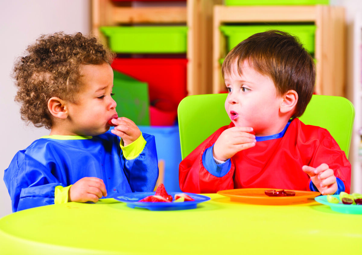 Two toddlers in bibs eating at a table
