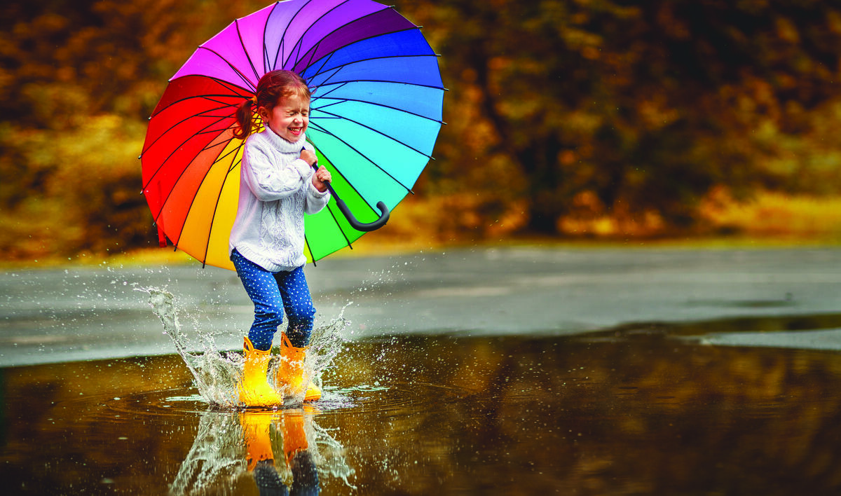 Girl with rainbow umbrella jumping in puddle