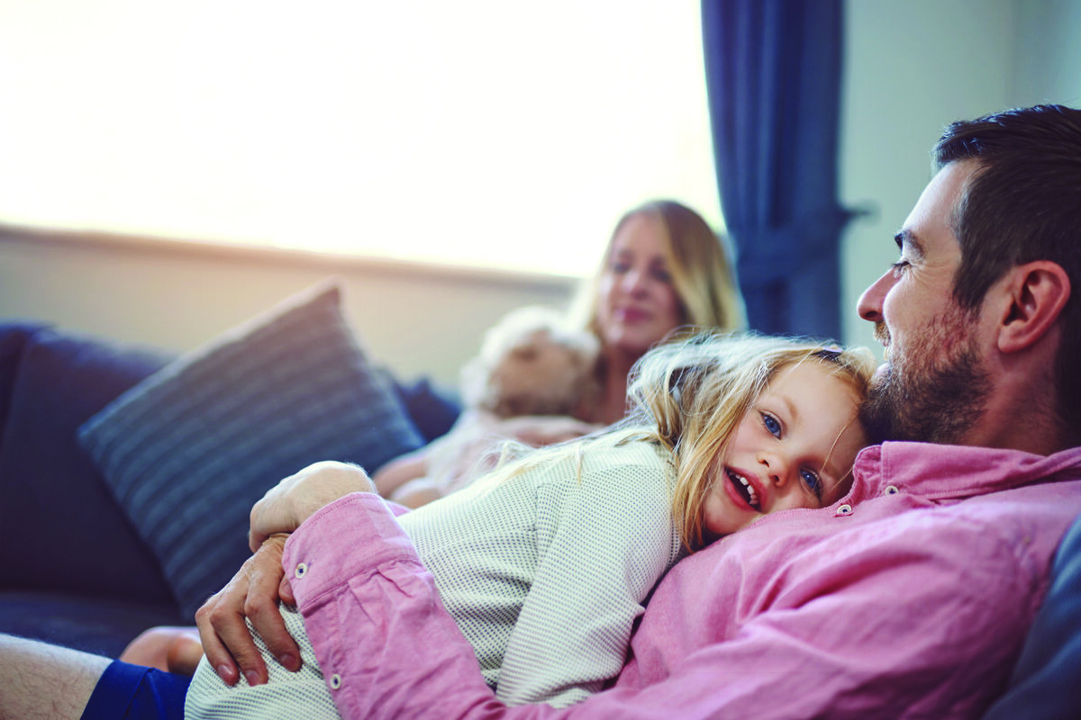 Father comforting young daughter on couch